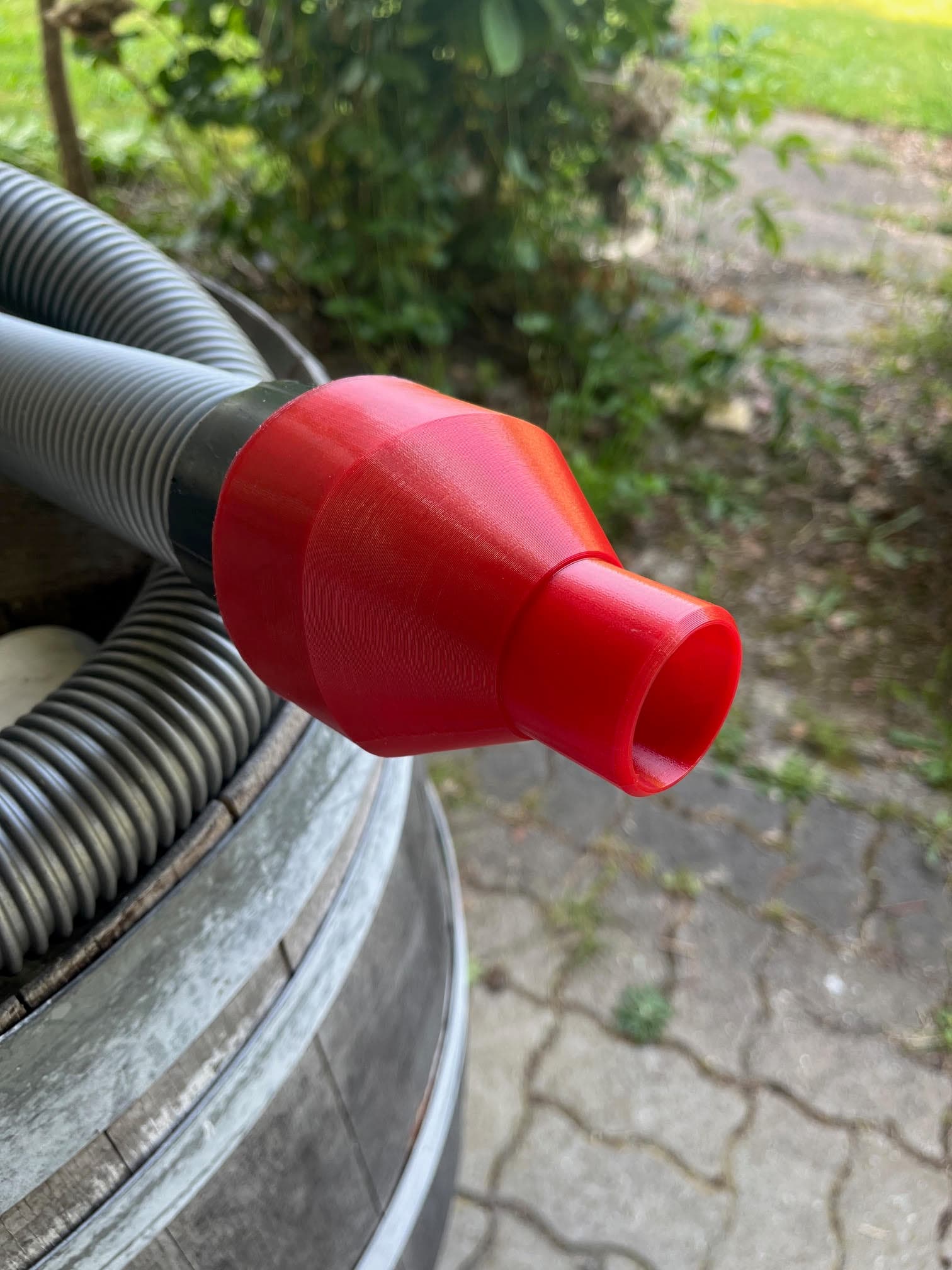 Buse rouge imprimée en 3D fixée à un tuyau flexible gris dans un jardin.