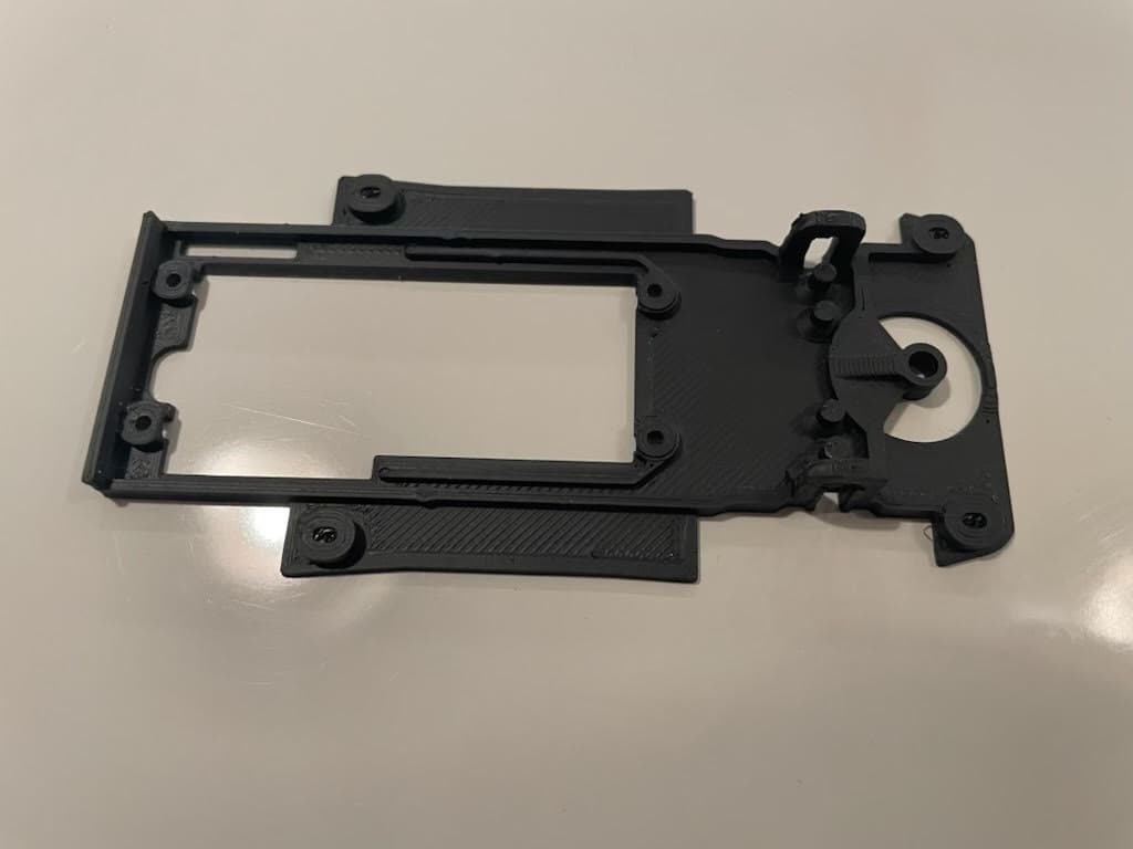 Châssis noir imprimé en 3D avec trous de fixation et découpe rectangulaire sur surface claire.