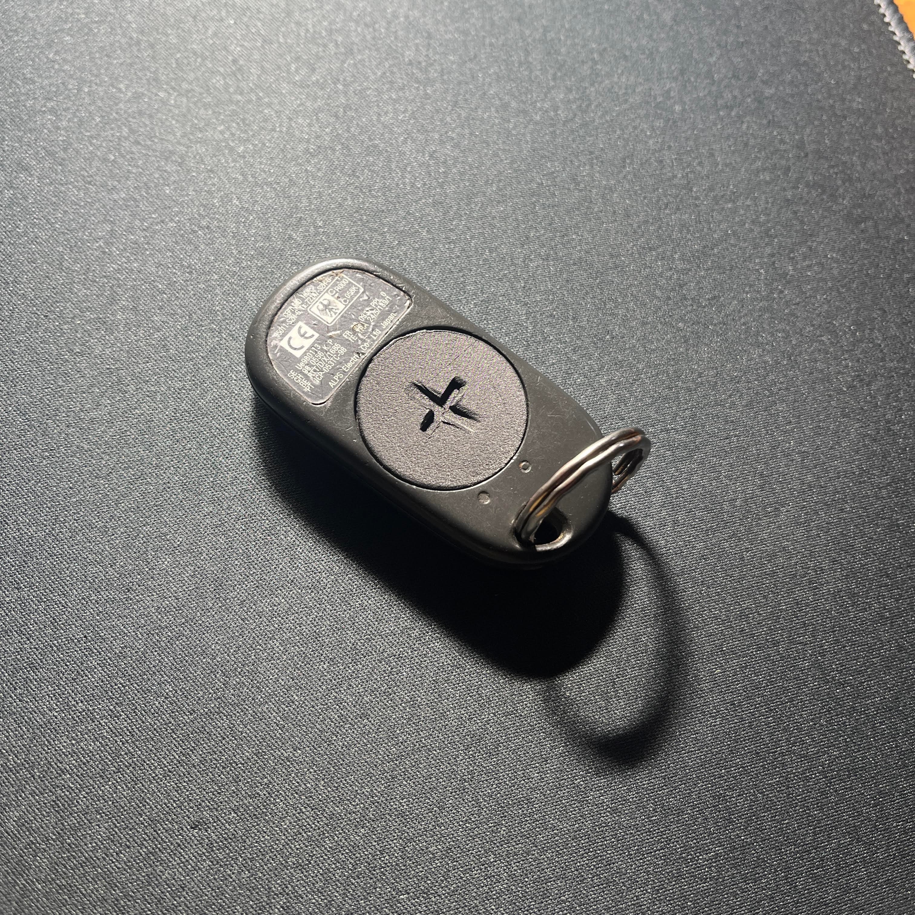 Télécommande de voiture noire avec couvercle de pile circulaire sur une surface texturée sombre.