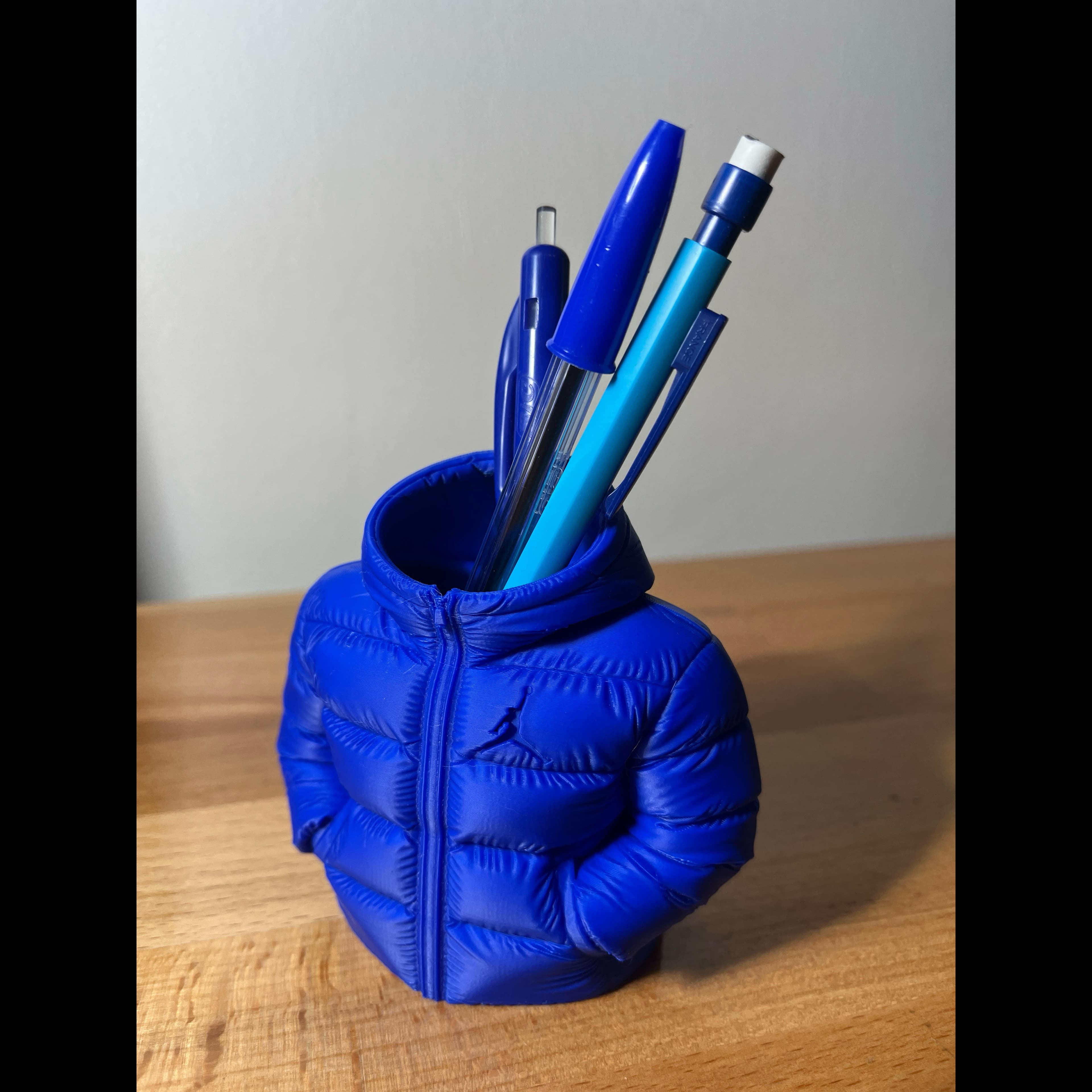 Porte-stylos bleu en forme de doudoune miniature contenant des stylos et un crayon.