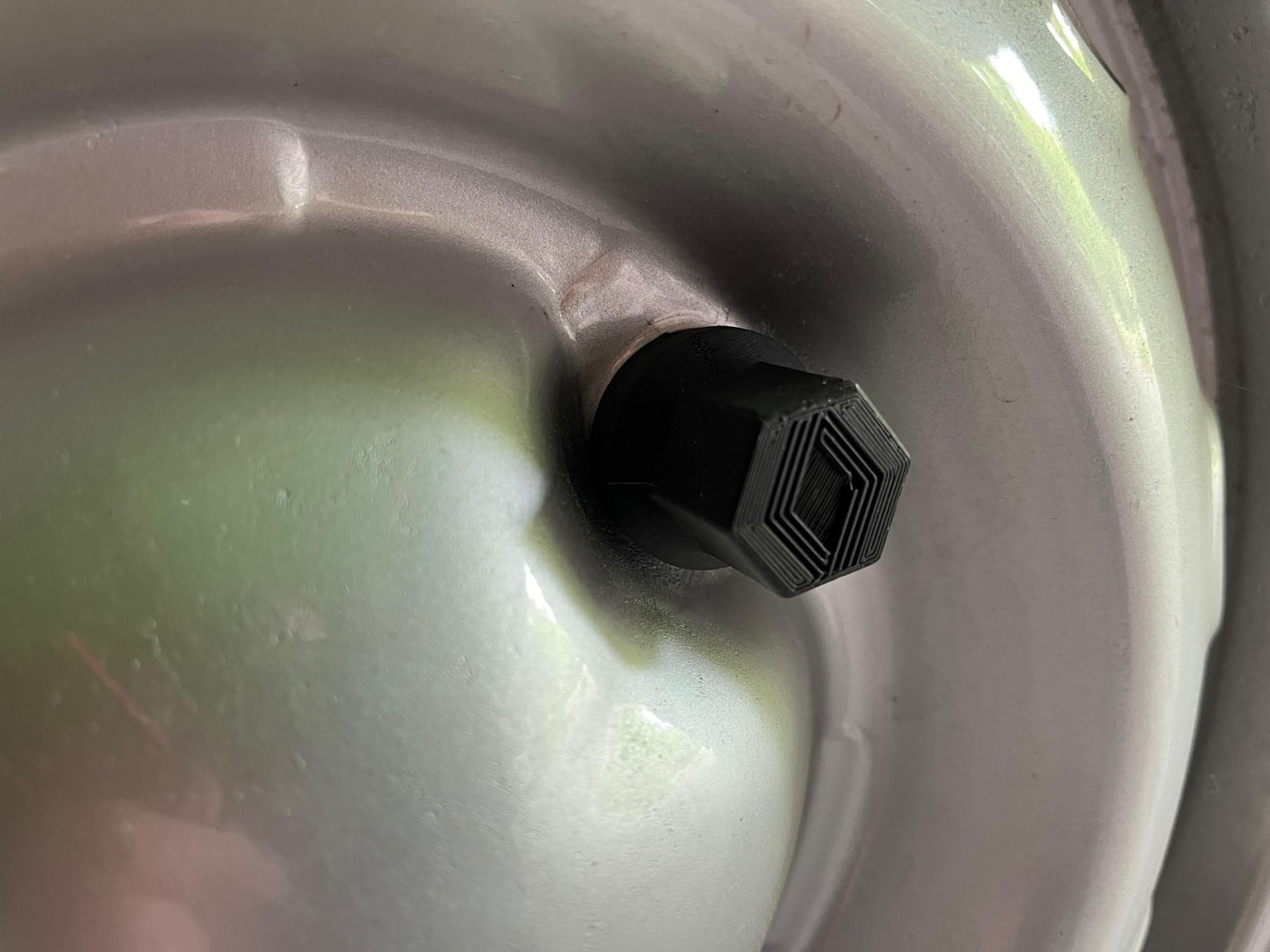 Bouchon de valve hexagonal noir avec un motif texturé sur une jante de roue argentée.
