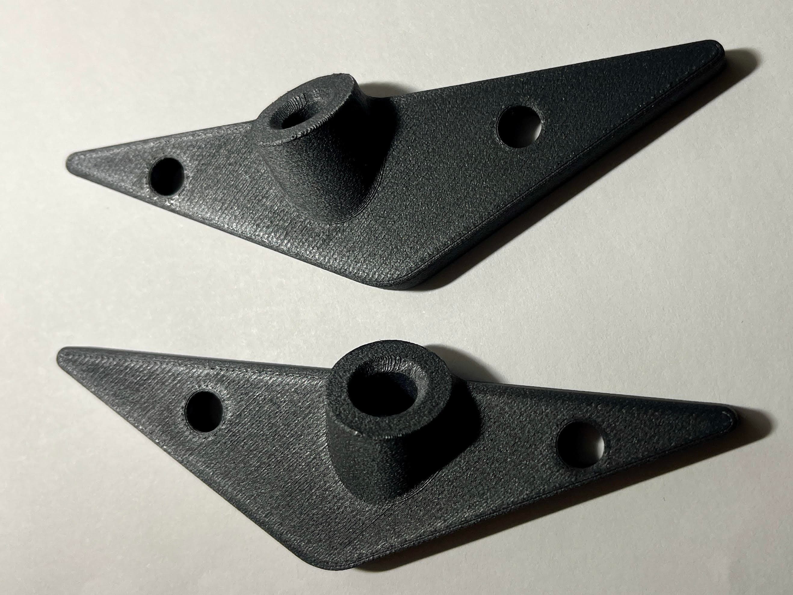 Deux pièces noires imprimées en 3D, triangulaires avec des trous, sur une surface blanche.