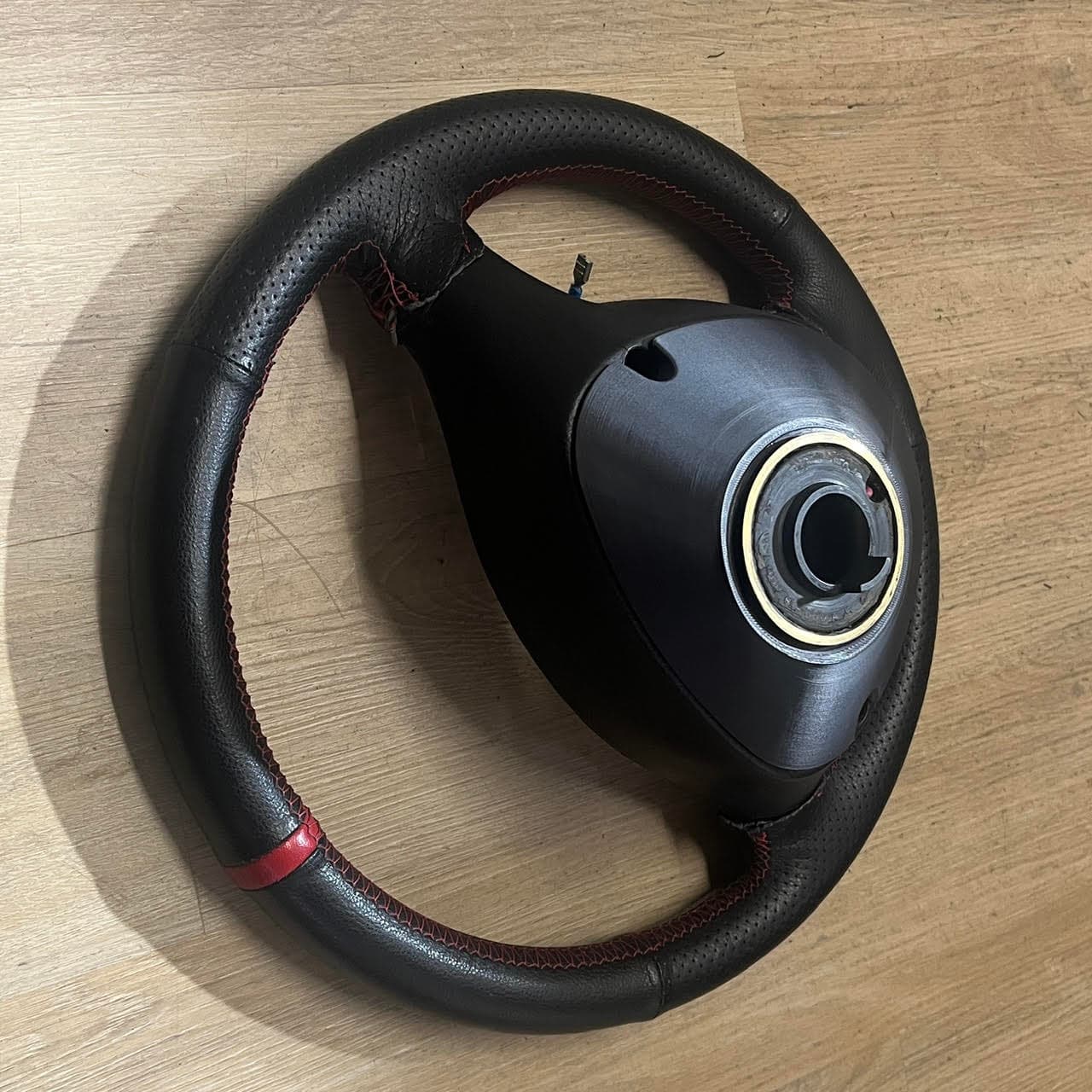 Volant en cuir noir avec surpiqûres et bande rouges sur un parquet en bois clair.