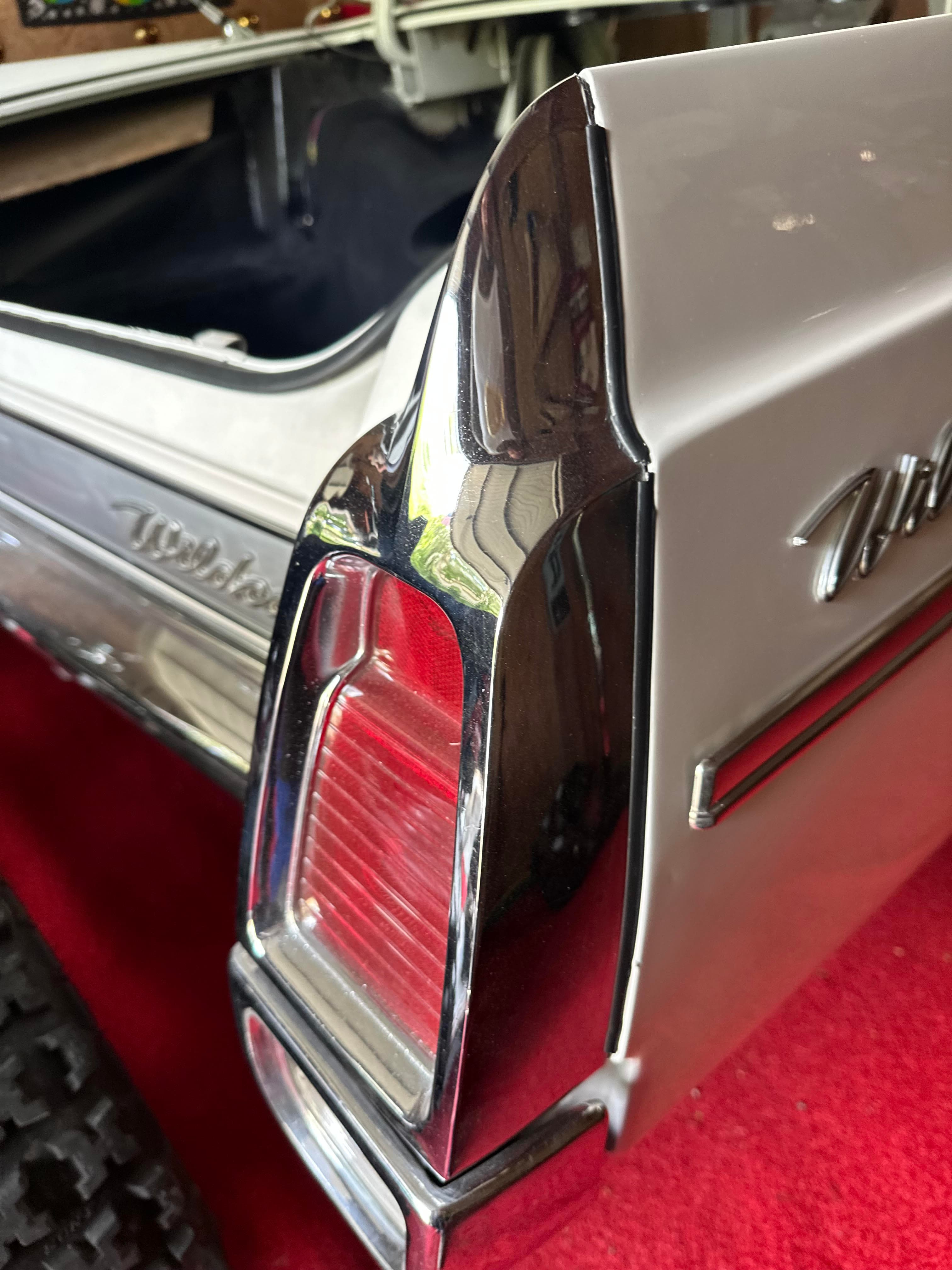 Détail du feu arrière chromé d'une Buick Wildcat blanche classique sur un tapis rouge.